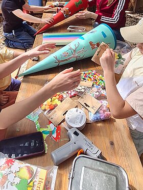 Kinder- und Erwachsenenhände die an einer Schultüte basteln.