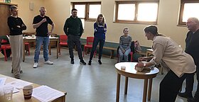Teilnehmergruppe steht im Halbkreis und beobachtet eine Teilnehmerin an der Reanimationsbabypuppen.