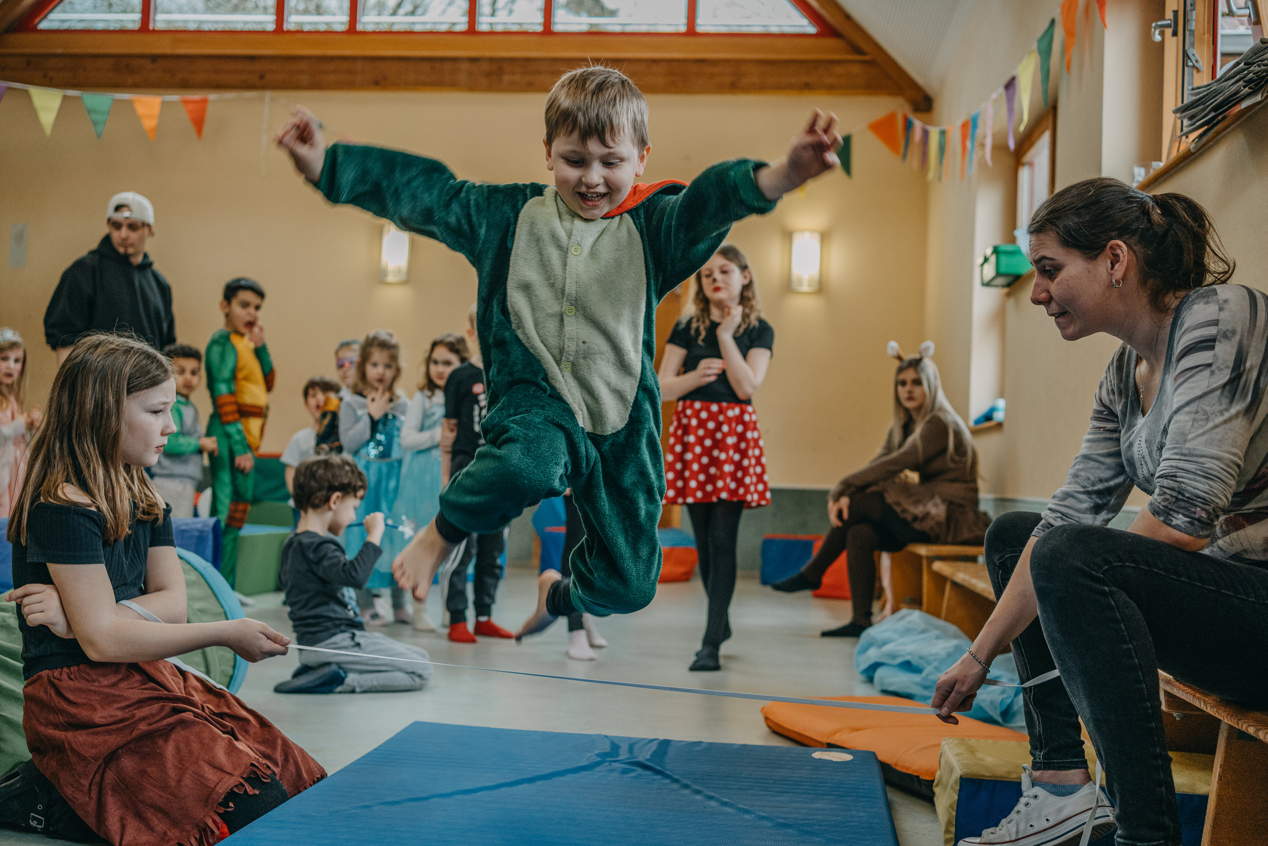 Verkleidete Kinder bei der Faschingfeier. In der Mitte springt ein Kind fröhlich auf die Kamera zu.