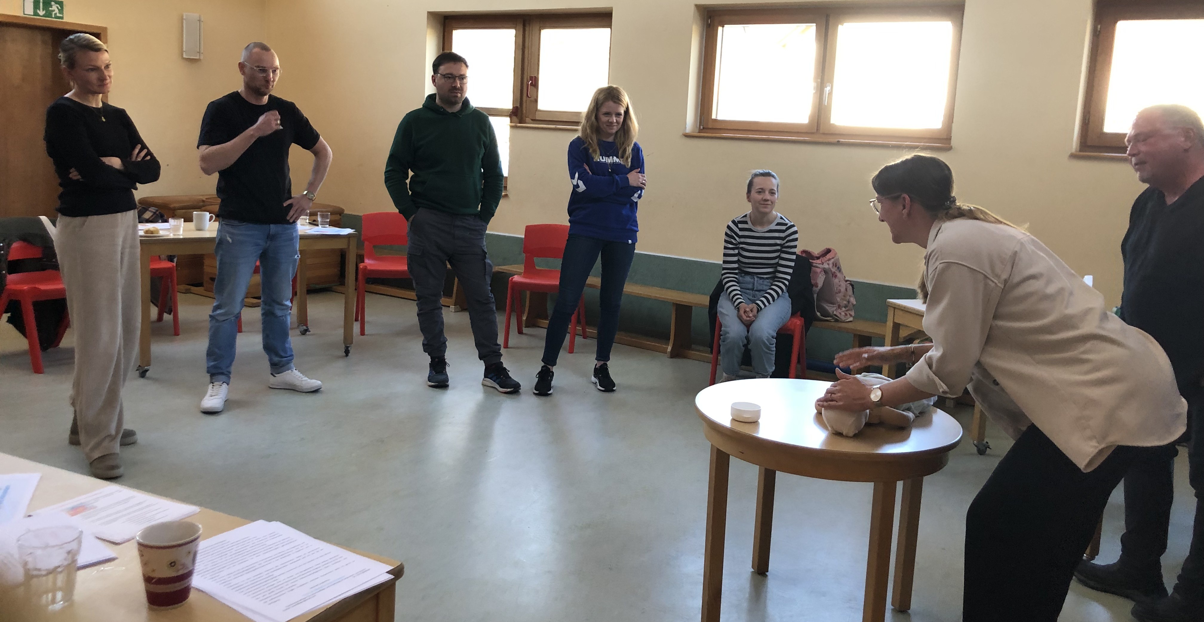 Teilnehmergruppe steht im Halbkreis und beobachtet eine Teilnehmerin an der Reanimationsbabypuppen.