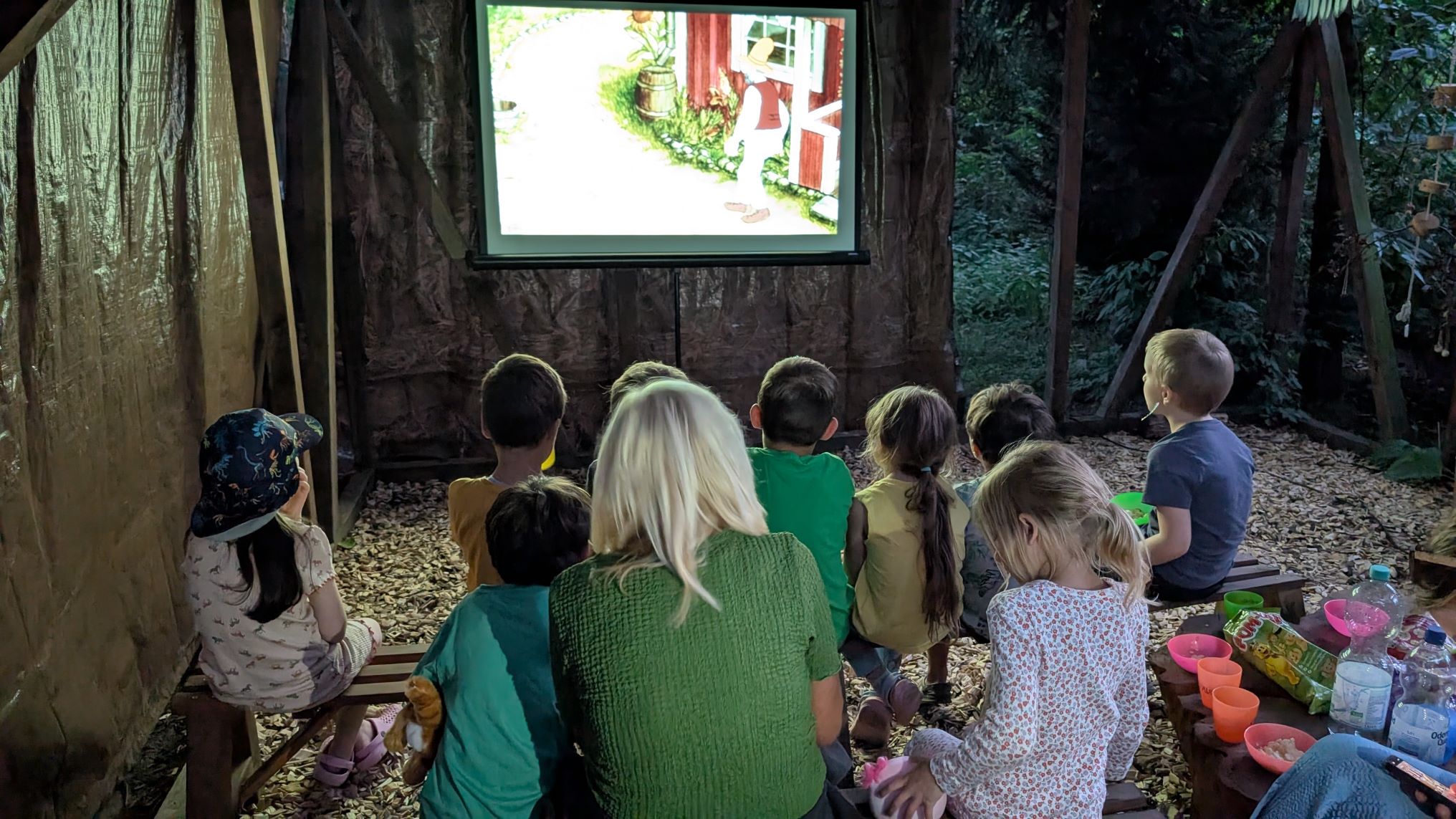Waldkindergartenkinder vor der Leinwand. Im Waldkino läuft Peterson und Findus.
